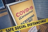A yellow A-frame sign that says COVID-19 screening clinic.