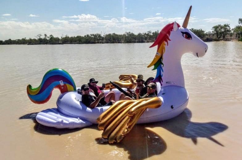 People sit inside a large inflatable unicorn on a lake.