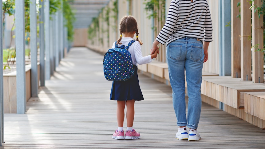 A woman holding the hand of a young girl who is carrying a backpack on her back.