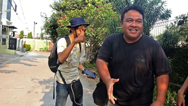 Indonesian filmmaker Dandhy Laksono smiles and gestures as journalists take photos of him.