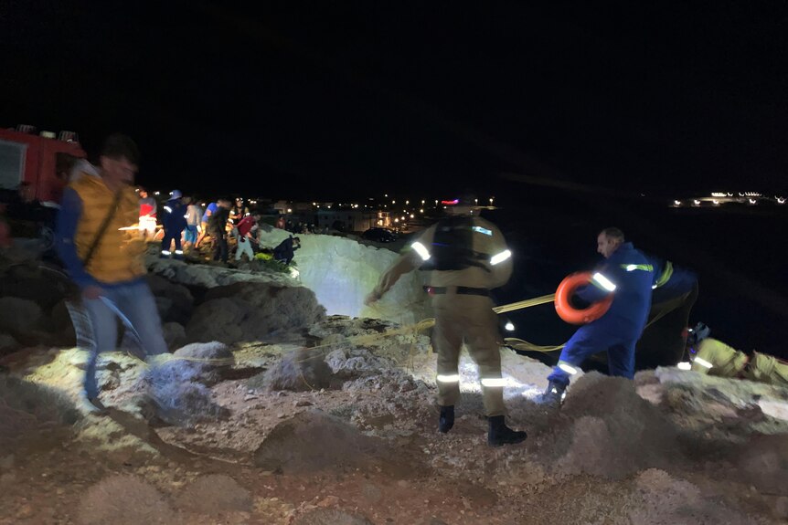 Authorities and local residents walk along a cliff face at night looking for survivors from a shipwreck