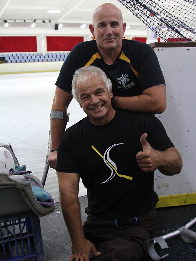 Two men from Brisbane's para ice hockey team standing in front of the entrance to the ice at a skating rink.