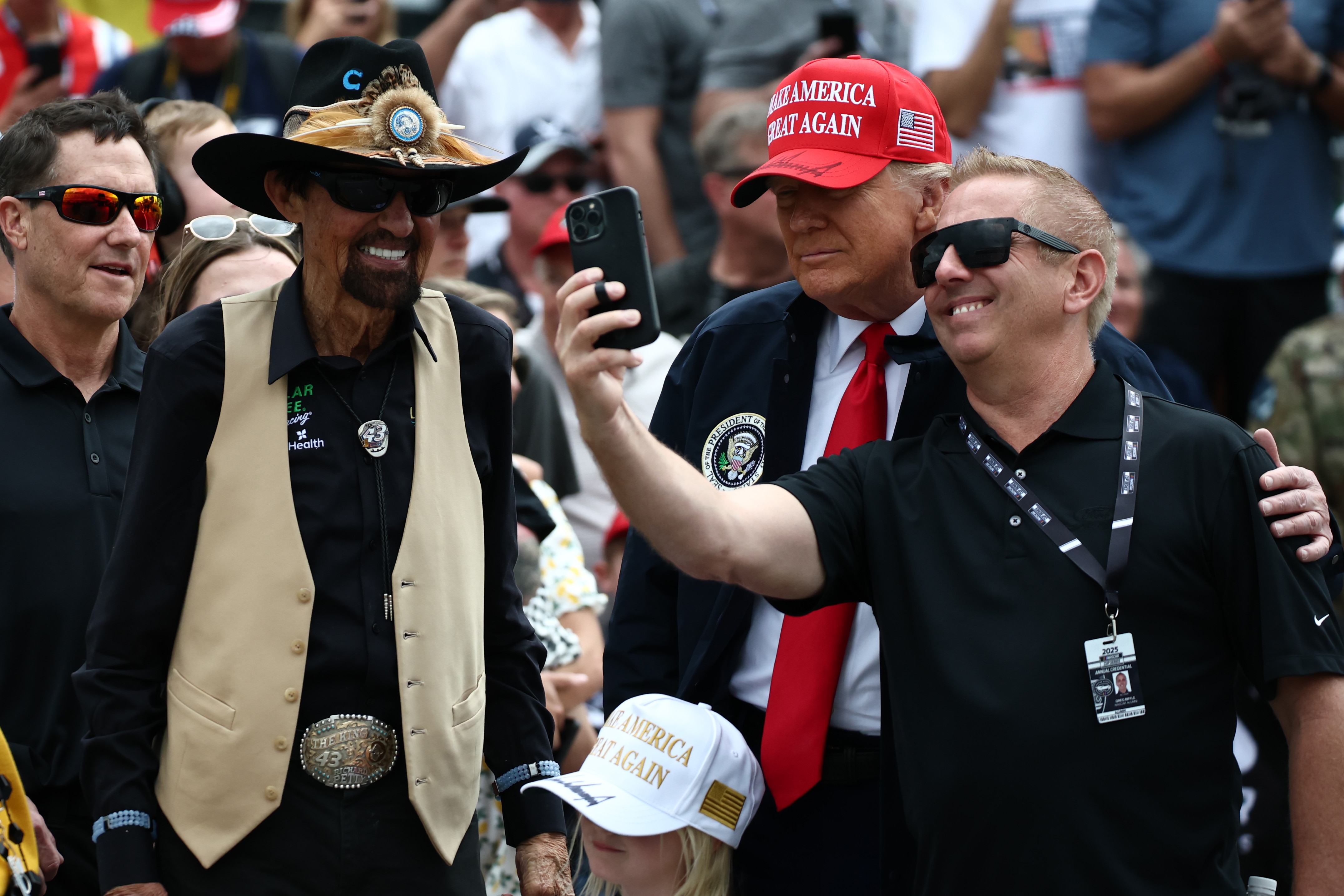 Greg Biffle tira uma selfie com Trump, que usa boné vermelho, gravata e terno. 