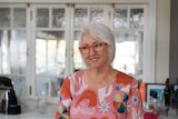A woman with silver hair, glasses, smiles away from the camera
