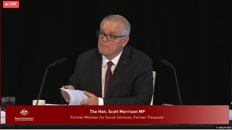 Morrison sits at a desk flicking through papers, looking at someone asking him questions