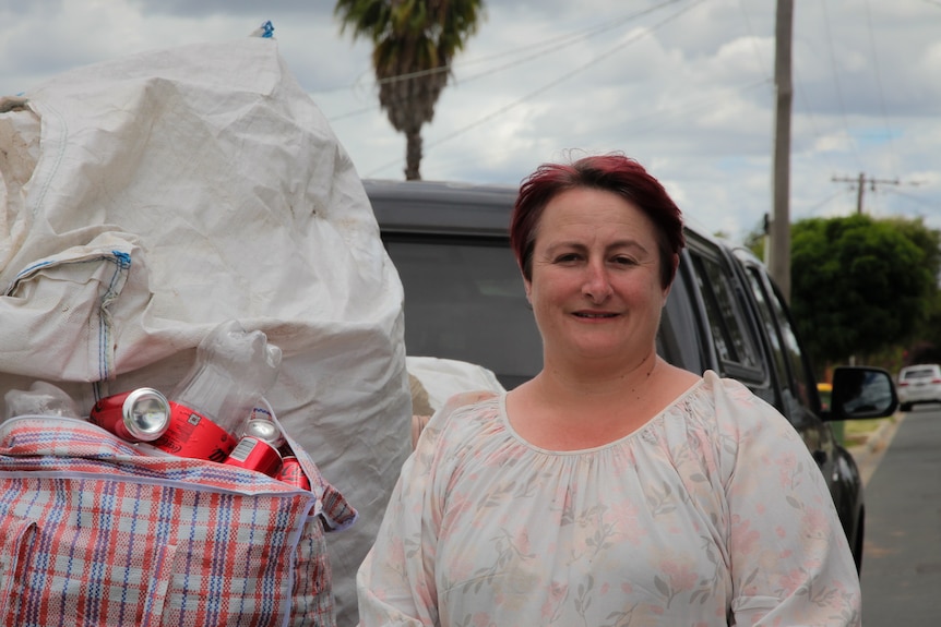 A woman with short red hair in a white blouse standing by large bags filled to the brim with empty cans.