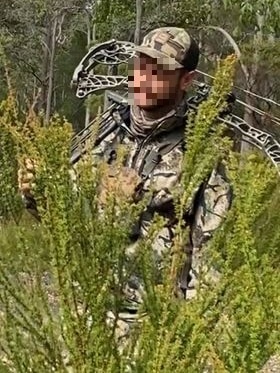 a man carries a compound bow through bushland