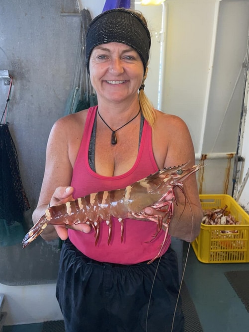A mid shot of a woman holding a giant prawn the size of a forearm