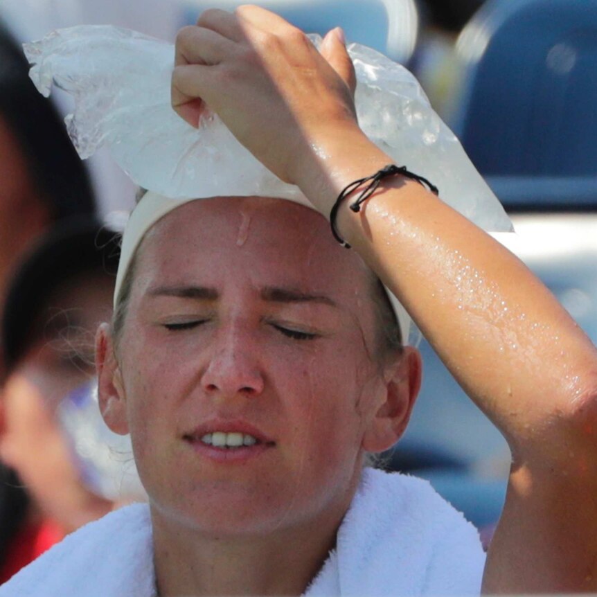 A female tennis player sits with her eyes closed, holding a bag of ice on her head.