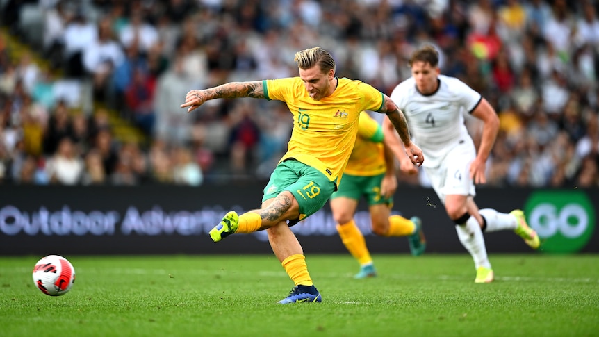 A soccer player wearing yellow and green shoots the ball during a game