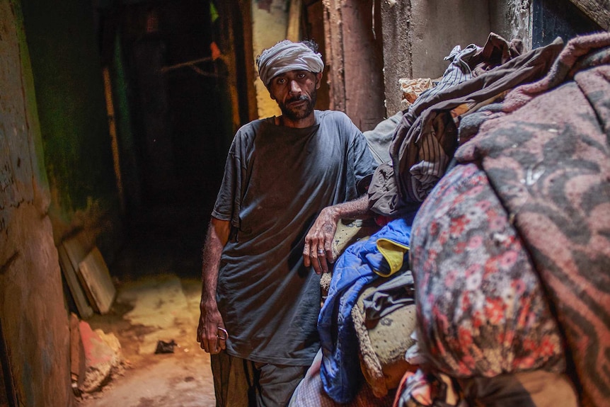 Mohamed with a pile of mattresses and bedding