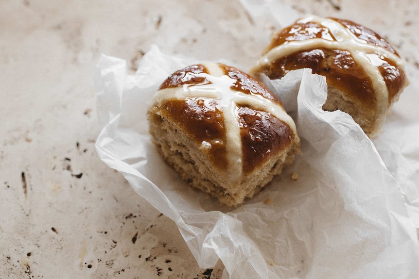 Two homemade hot cross buns on baking paper, an Easter baking project during coronavirus.