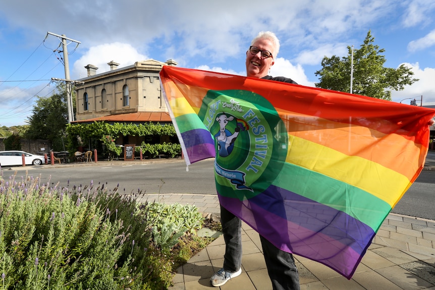 ChillOut Festival director Merryn Tinkler holding a large Rainbow flag.