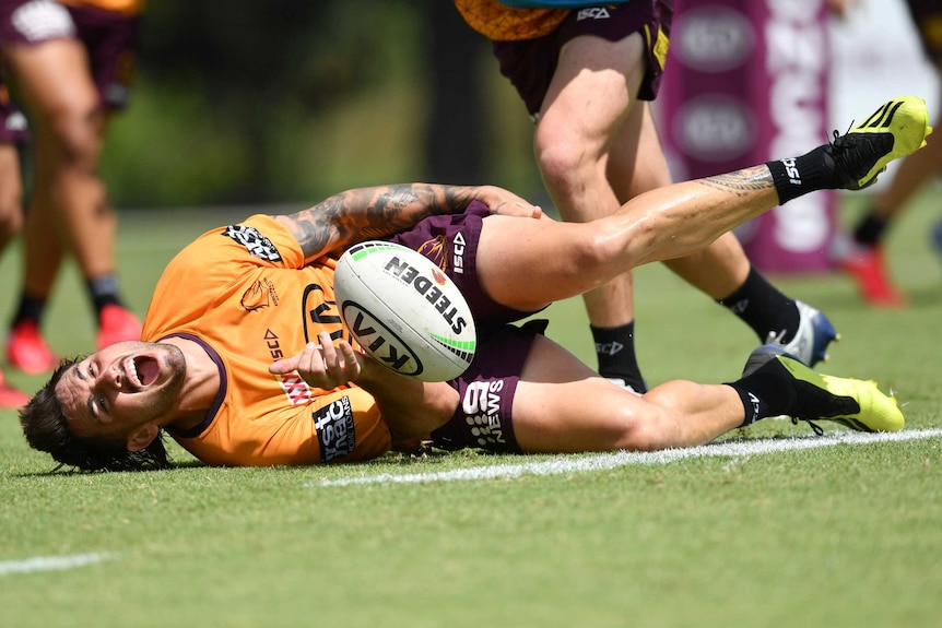 A male Brisbane Broncos player lies on the ground clutching his leg after injuring his knee at an NRL training session.