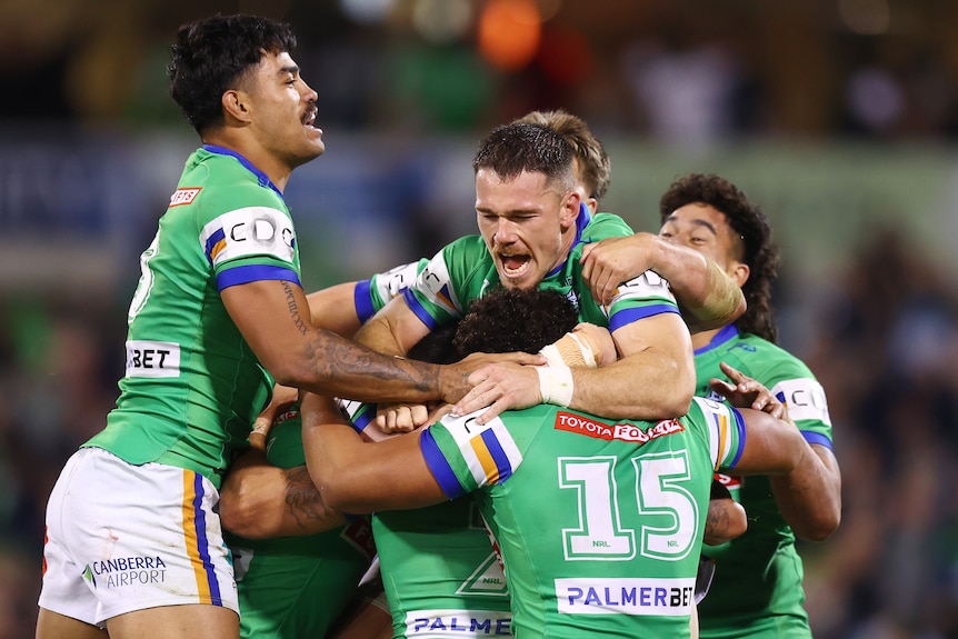 Raiders players jump on Jamal Fogarty in celebration after wining an NRL game.
