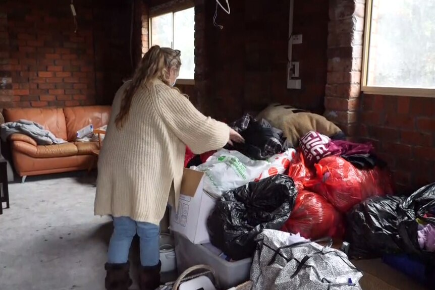 A woman stacks plastic bags full of clothes in a room with the flooring and walls stripped back