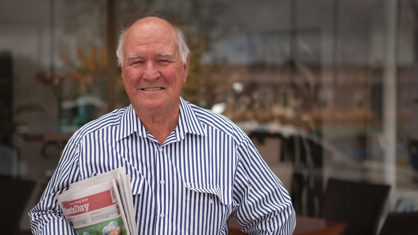 Tony Windsor stands outside a shopfront holding a newspaper