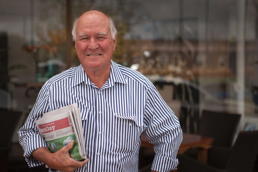 Tony Windsor stands outside a shopfront holding a newspaper