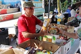 Man in red shirt, black cap handing out food at market.