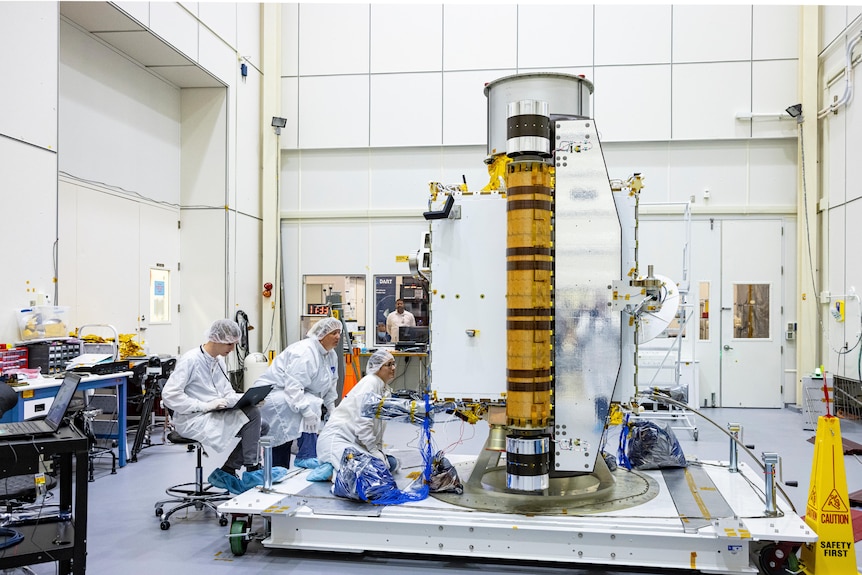 People in white coats inspect a spacecraft inside a laboratory.