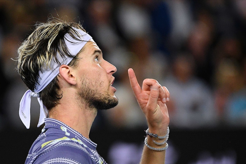 A tennis player points with one finger in the air as he looks at the umpire.