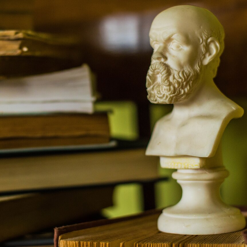 An alabaster bust of Socrates sits next to a pile of books.