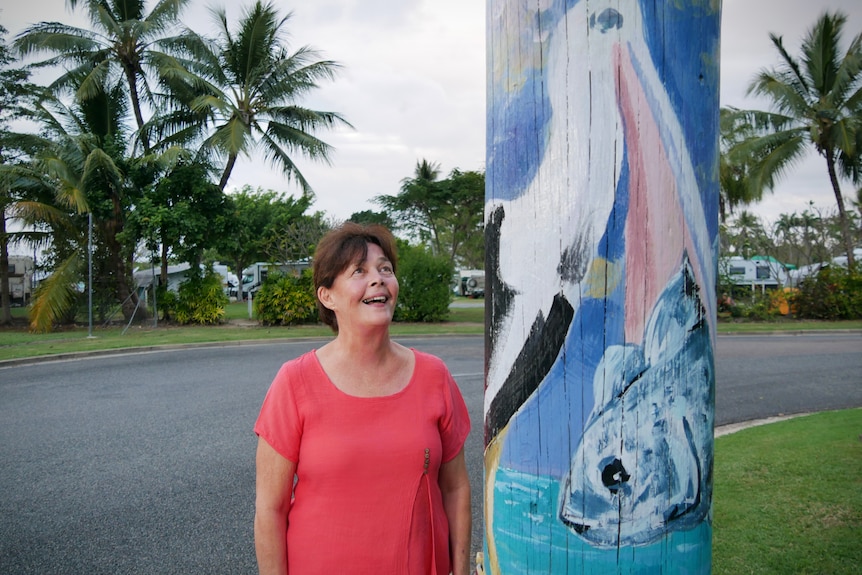 A smiling woman looks at a painted power pole on a street corner