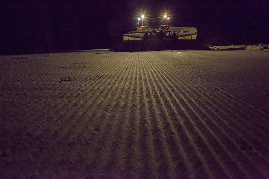Corrugations in the snow are illuminated by the lights of a snow grooming machine as it grades the slopes in the dark.