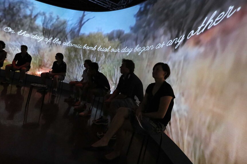 An audience is silhouetted against an immersive installation that integrates original artwork with atomic survivor stories.