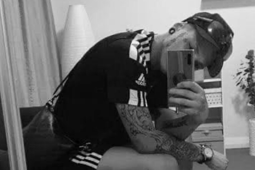 A woman in adidas clothes, cap and tattoos and stretchers takes a selfie.
