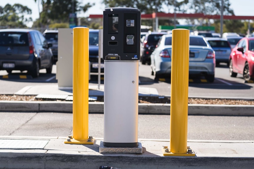 A grey and white parking ticket machine between two yellow bollards.