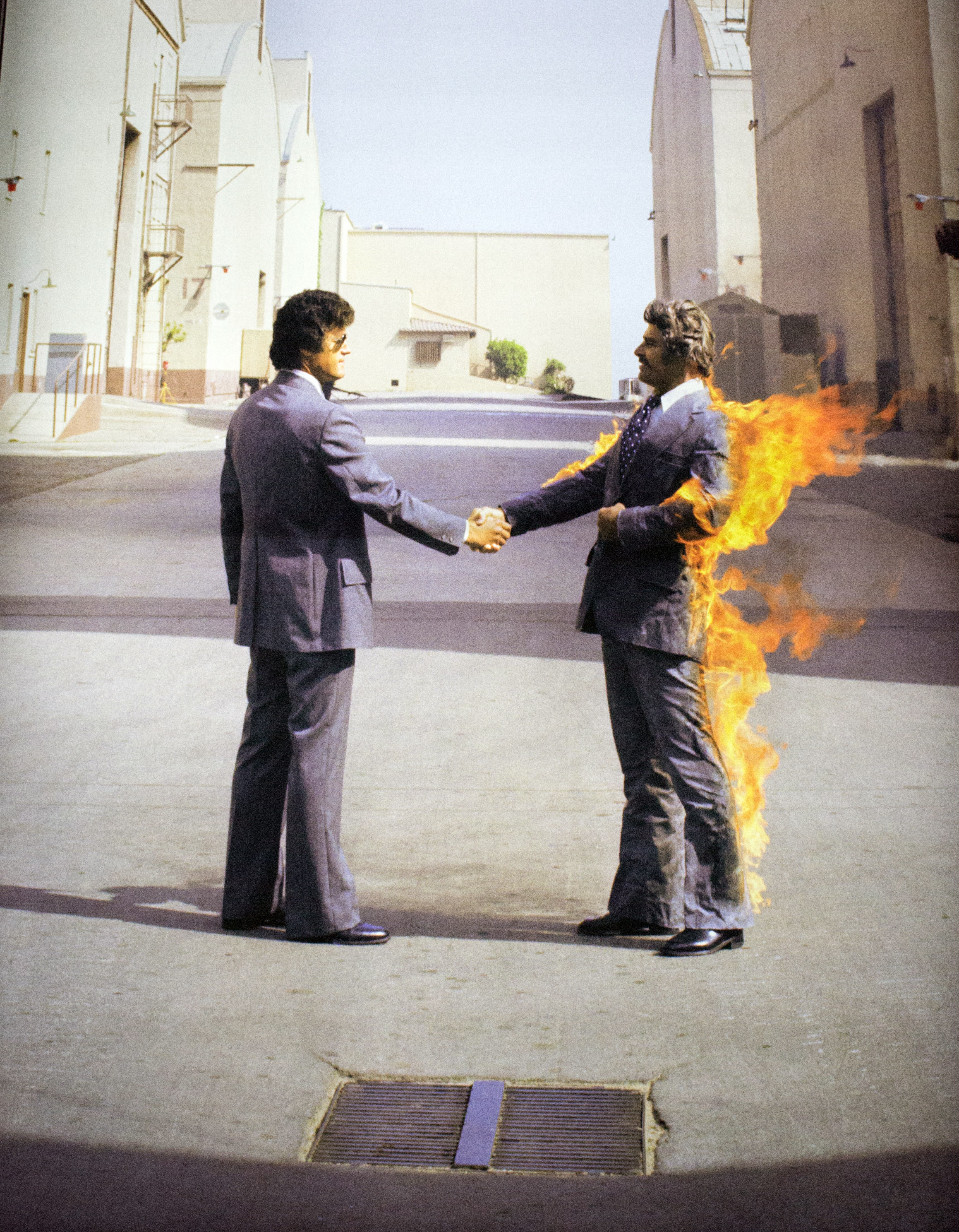 an album cover showign two men in 70s suits shaking hands, one of them is on fire