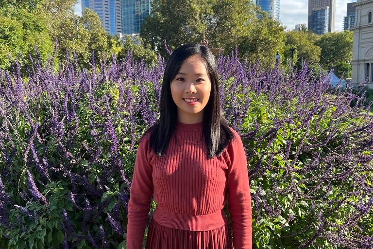 A profile image of Irene Teo with red dress, long lack straight hair, smiling, in front of purple flowered bush