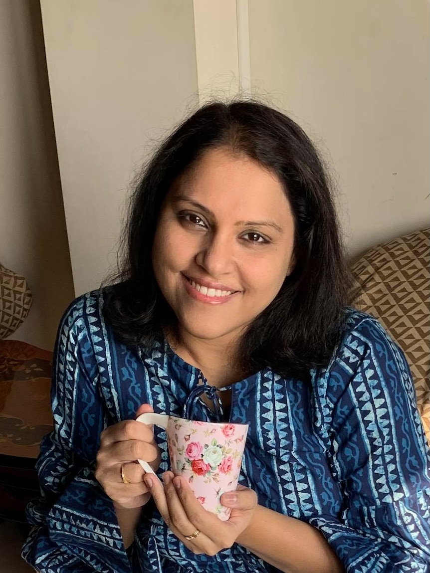 A woman holding a cup of tea and smiling.