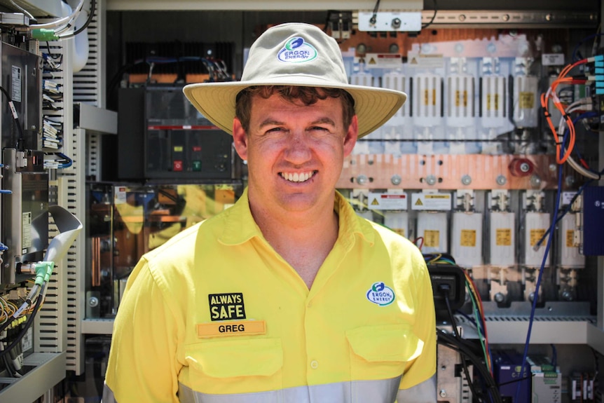 Ergon Energy Engineer Greg Elkins in high vis workwear, stands in from of a transmitter.