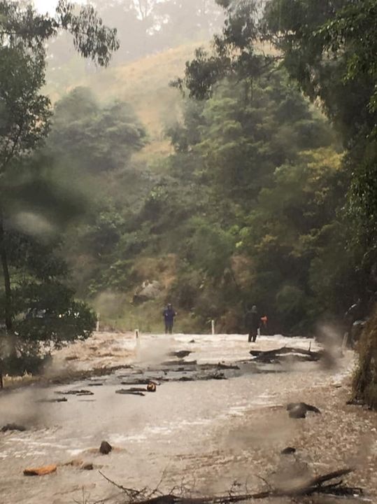 Picture showing brown flood water covering a road, surveyed by people in raincoats.