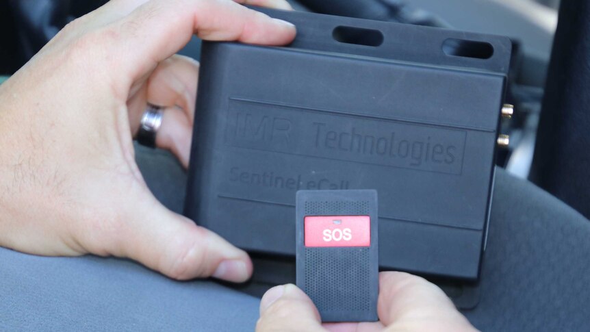 Close up of a man holding the Sentinel emergency beacon device, which consists of a sturdy black box and SOS remote.