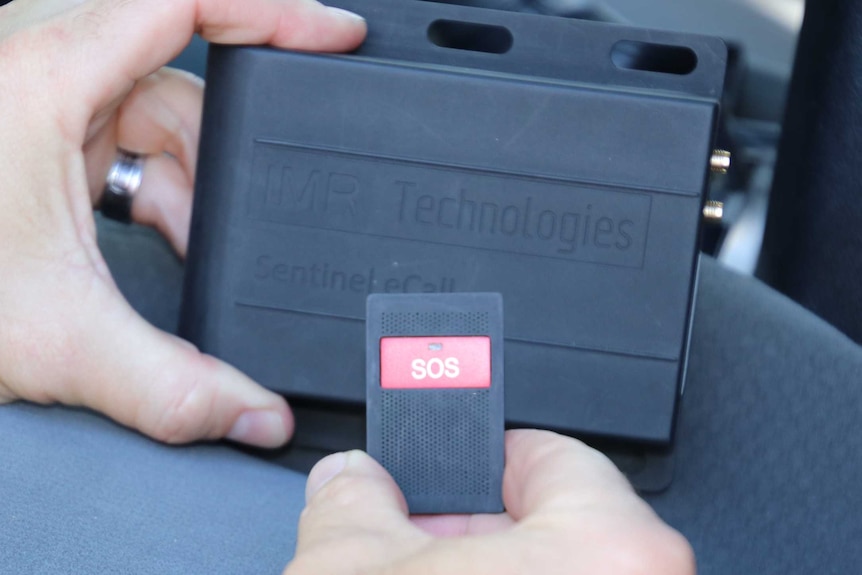 Close up of a man holding the Sentinel emergency beacon device, which consists of a sturdy black box and SOS remote.