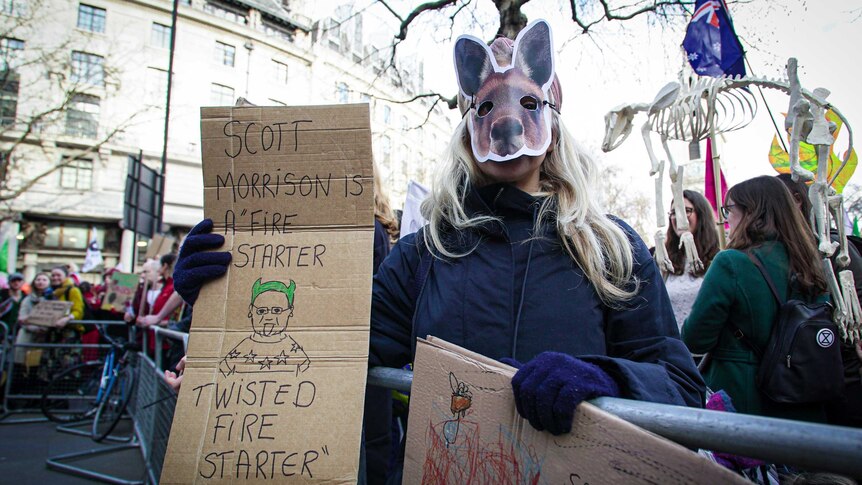 a woman with a kangaroo mask holds a sign reading 'Scott Morrison is a fire starter twisted fire starter'