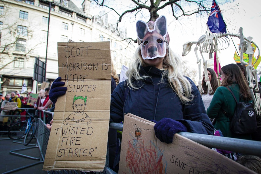 a woman with a kangaroo mask holds a sign reading 'Scott Morrison is a fire starter twisted fire starter'