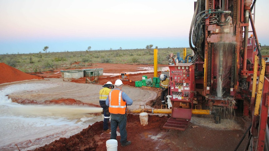 Workmen next to a large bore drilling for water with water spilling onto the red earth.