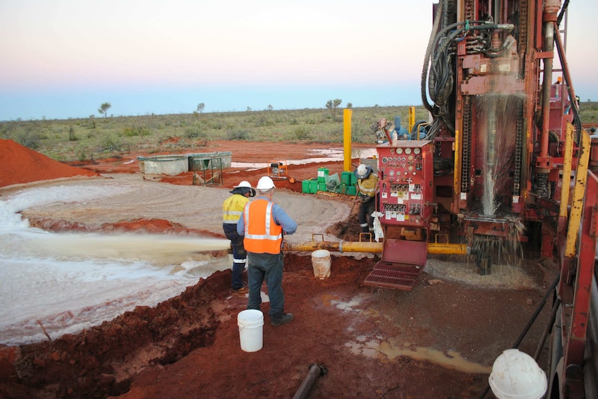 Workmen next to a large bore drilling for water with water spilling onto the red earth.