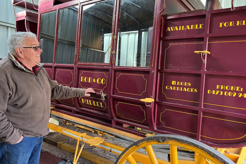 Man looking at a red carriage Rob and Co carriage with yellow writing 