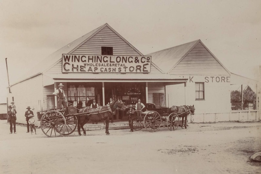 Black and white photograph of the Wing Hing Long store building with men and horses out front.