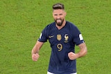 Soccer player in navy jersey holds out fists in celebration on pitch.