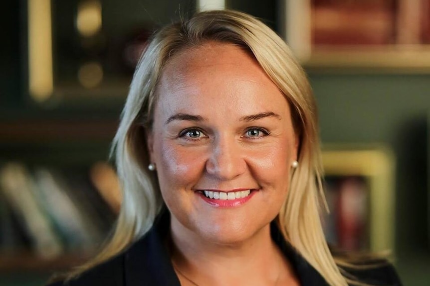 A woman with blonde hair and wearing a dark jacket, smiling.