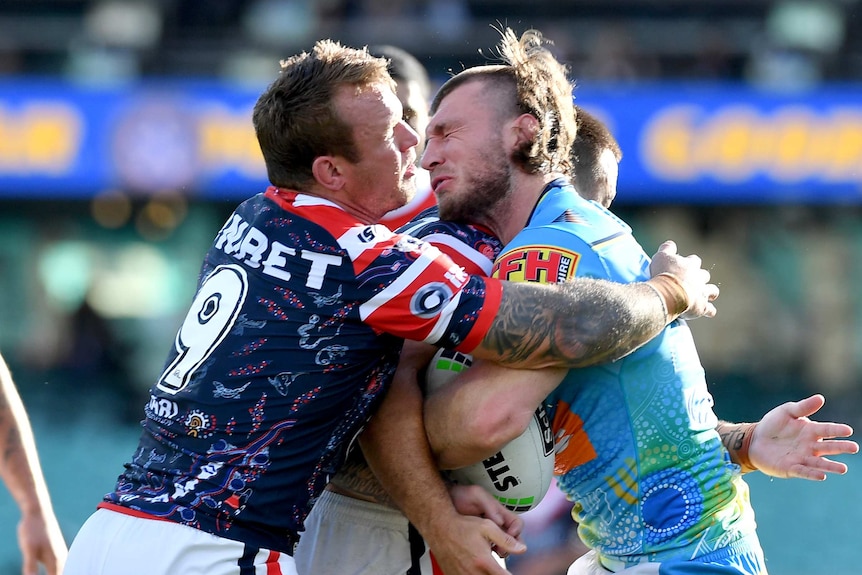 A Sydney Roosters NRL player tackles a Gold Coast Titans opponent holding the ball around the chest area.