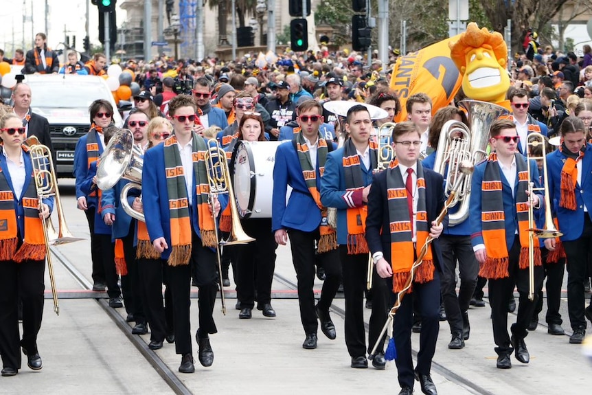 A marching band with the colours of the Greater Western Sydney Football Club moves down the street.