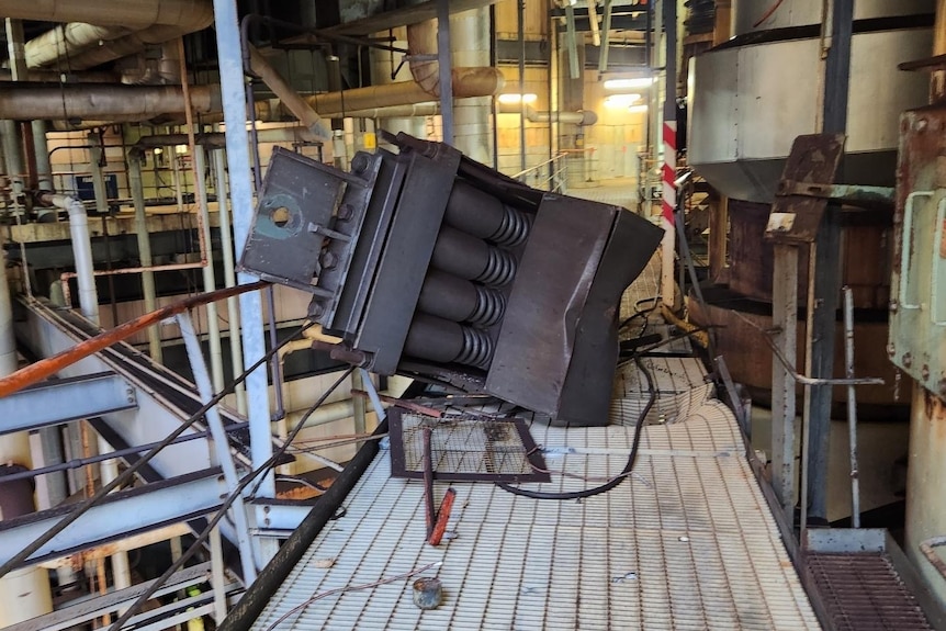 Truck-sized piece of metal that is lying on a grid metal walkway after falling from an industrial ceiling