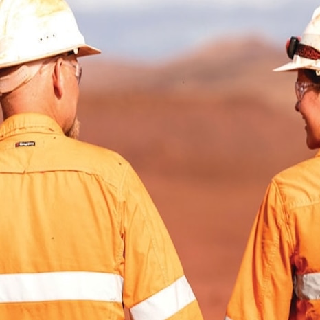 One male and one female mining worker wearing orange high vis stand with their backs to the camera